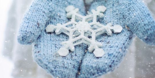 Blaue Wollhandschuhe, die einen Eiskristall halten.